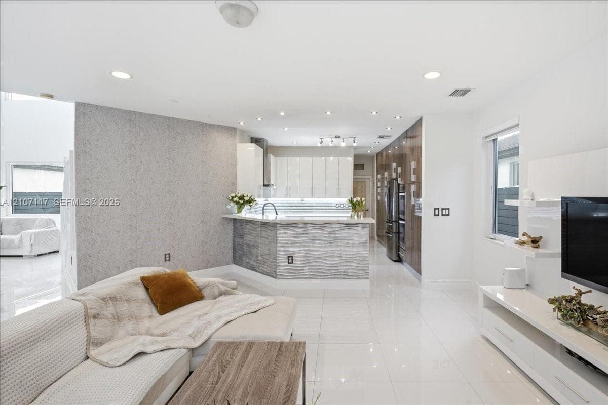 Open-concept kitchen featuring high-gloss cabinetry, a textured stone-finish island, integrated stainless steel appliances, recessed ceiling lighting, and polished tile flooring