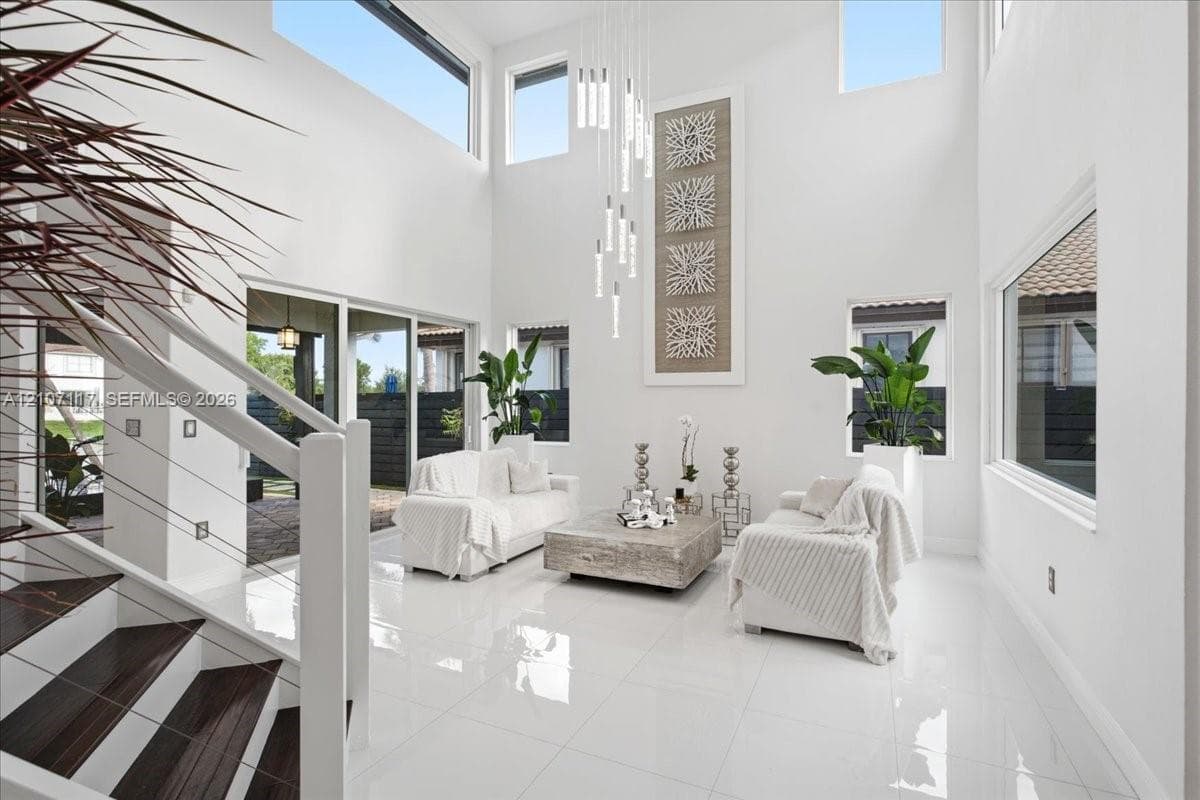 Double-height ceilings featuring tiered modern pendant lighting and multi-level windows, polished porcelain tile flooring, and a staircase with wood-finish treads and cable railing