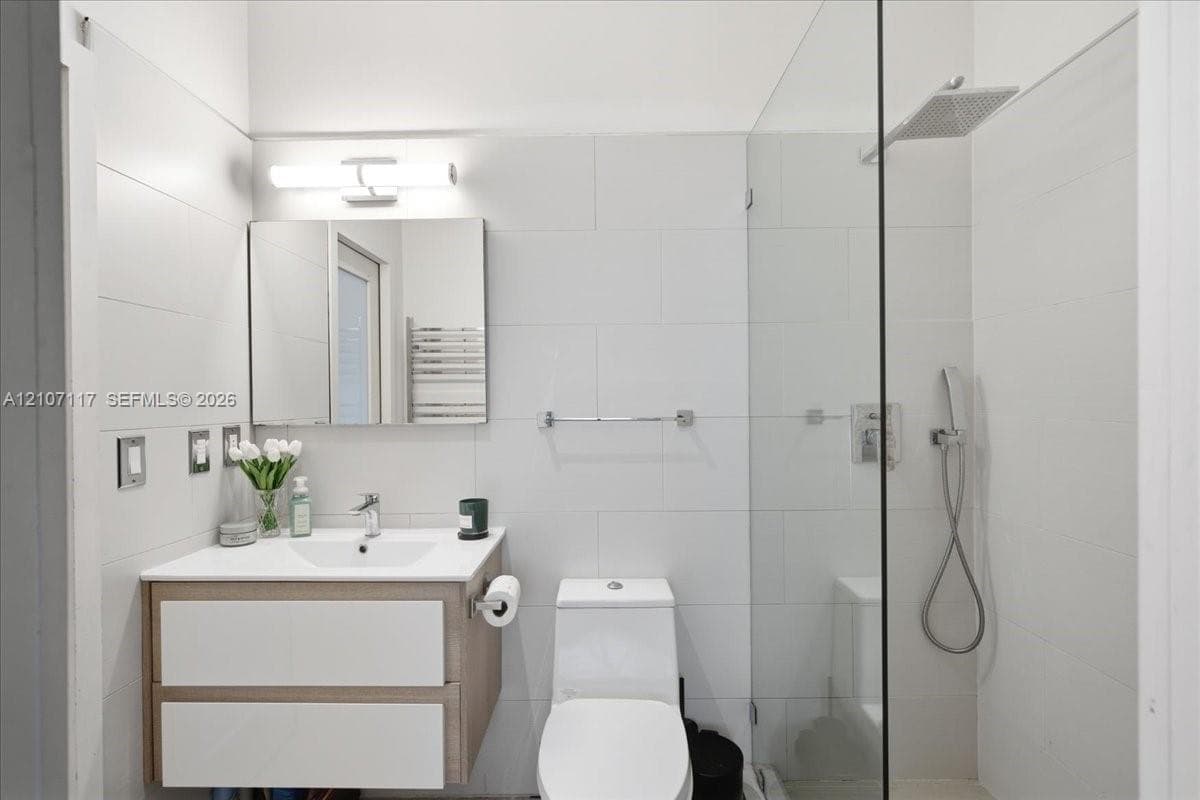 Floating wood-finish vanity with a white countertop, walk-in shower with a glass panel, rainfall shower head, handheld sprayer, and wall-mounted vanity lighting