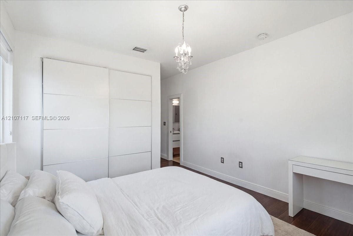 Room featuring dark wood-finish flooring, floor-to-ceiling built-in sliding door wardrobe, and a crystal chandelier