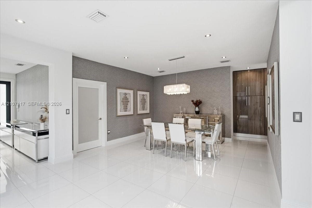 Open-concept interior featuring large-format polished tile flooring, textured wall coverings, a modern rectangular chandelier, and built-in full-height wood-finish cabinetry
