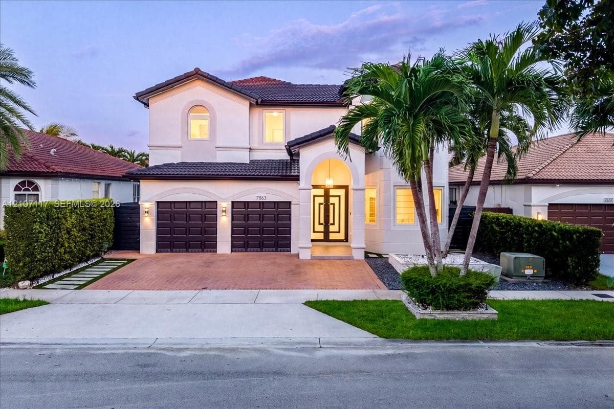 Two-story stucco exterior featuring a tiled roof, arched entryway, brick-paver driveway, double garage, and geometric-patterned glass front door
