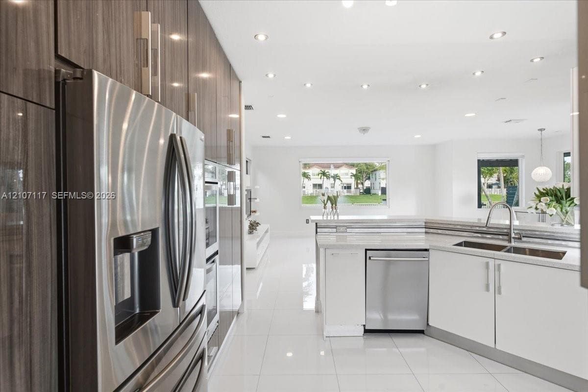 Modern kitchen featuring high-gloss, wood-grain cabinetry, stainless steel appliances, white stone countertops, integrated recessed lighting, and large-format porcelain tile flooring