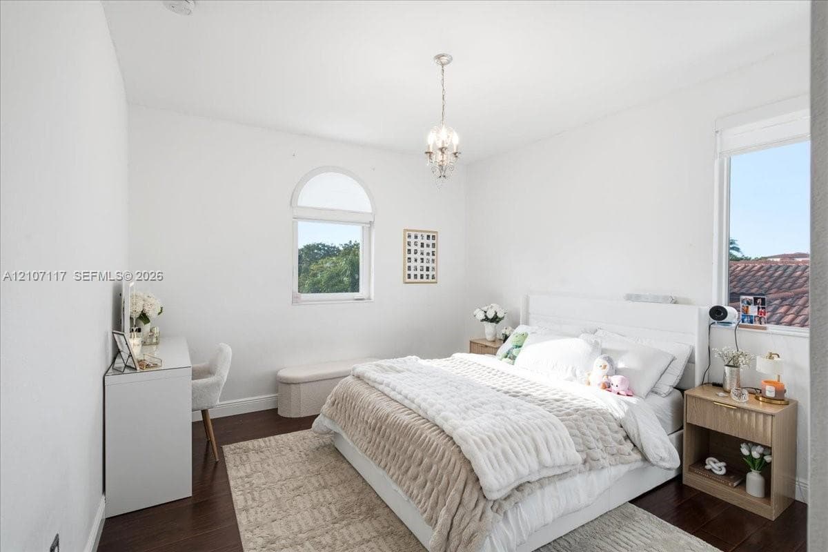 Room featuring wood-finish flooring, an arched window, and a central crystal-style chandelier