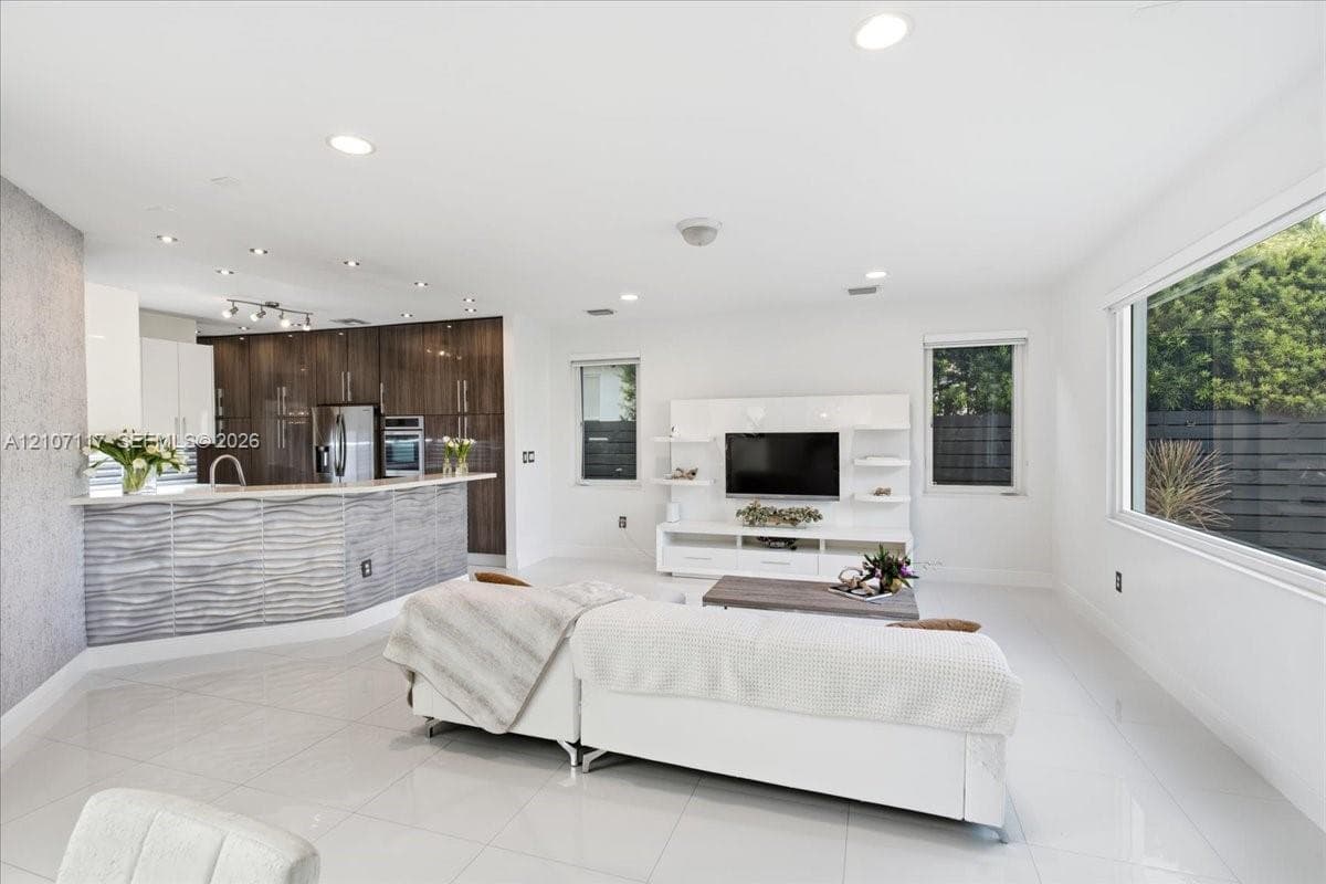 Open-concept interior featuring large-format tile flooring, recessed lighting, and a kitchen island with a textured, wave-patterned facade