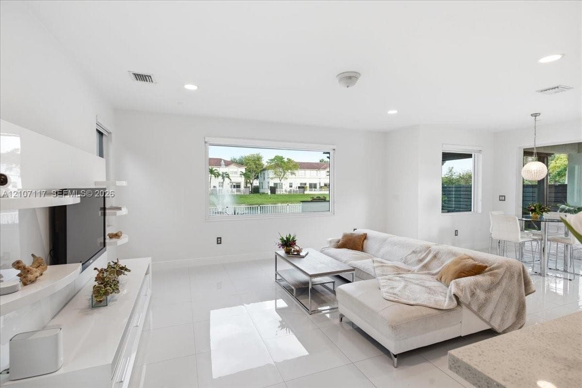 Open-concept living space featuring high-gloss tile flooring, recessed lighting, built-in media shelving, and large windows with water exposure