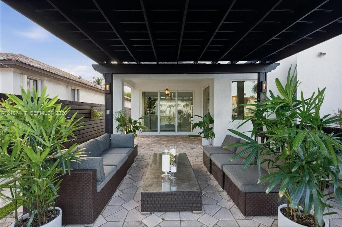 Outdoor patio featuring a black timber pergola, paved stone flooring, horizontal privacy fencing, and recessed exterior wall lighting
