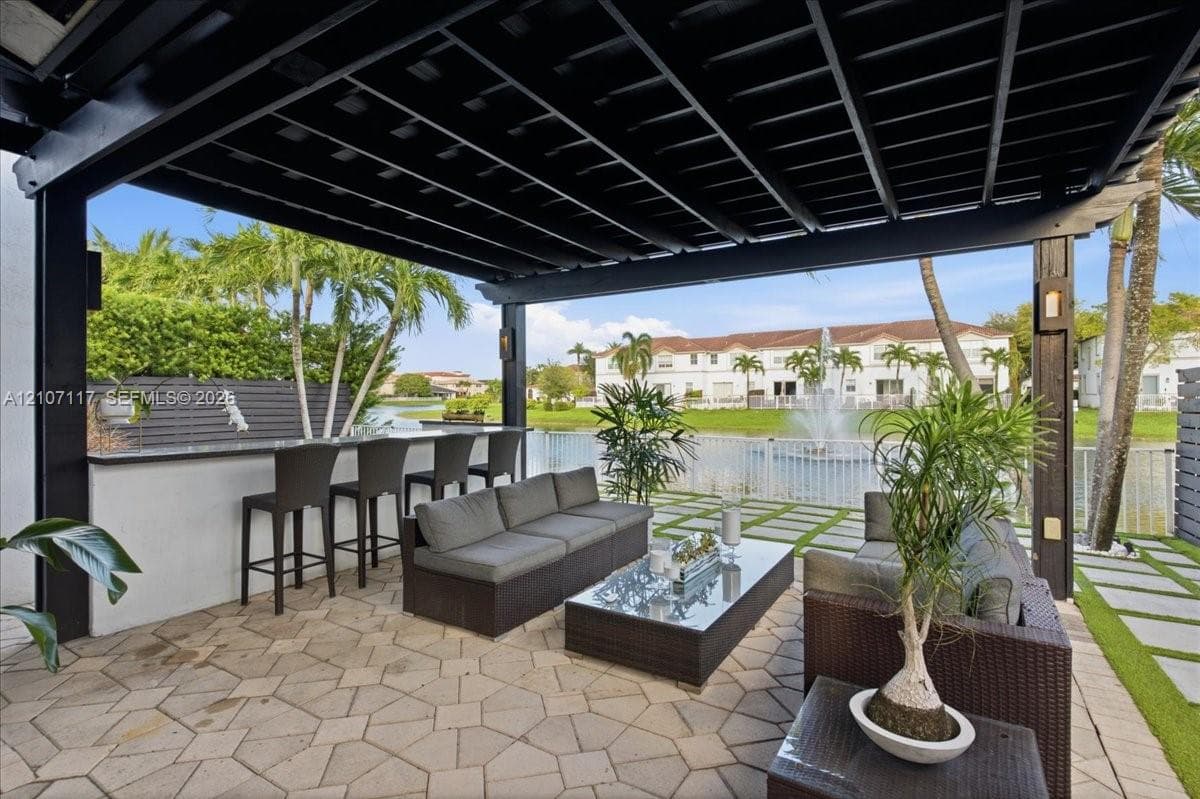 Covered patio featuring a black pergola, stone paver flooring, and a built-in outdoor bar with a stone countertop