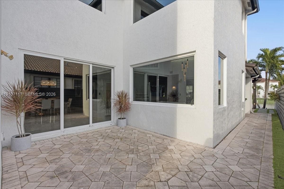 Exterior patio featuring geometric stone pavers, white stucco facade, expansive sliding glass door system, and large rectangular fixed-pane windows
