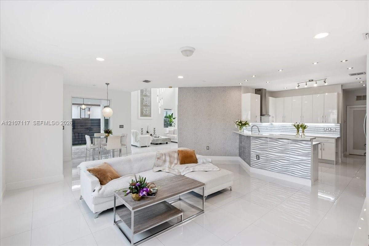Open-concept interior featuring large-format tile flooring, high-gloss kitchen cabinetry, a textured stone feature wall, and a raised breakfast bar with horizontal wave-patterned paneling