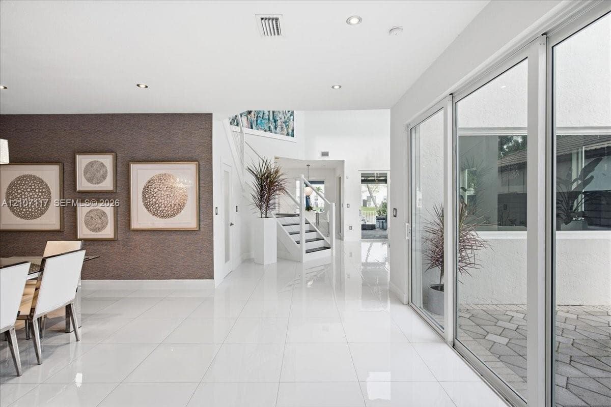 Polished tile flooring, textured accent wall, staircase with glass panel railing, and expansive sliding glass doors