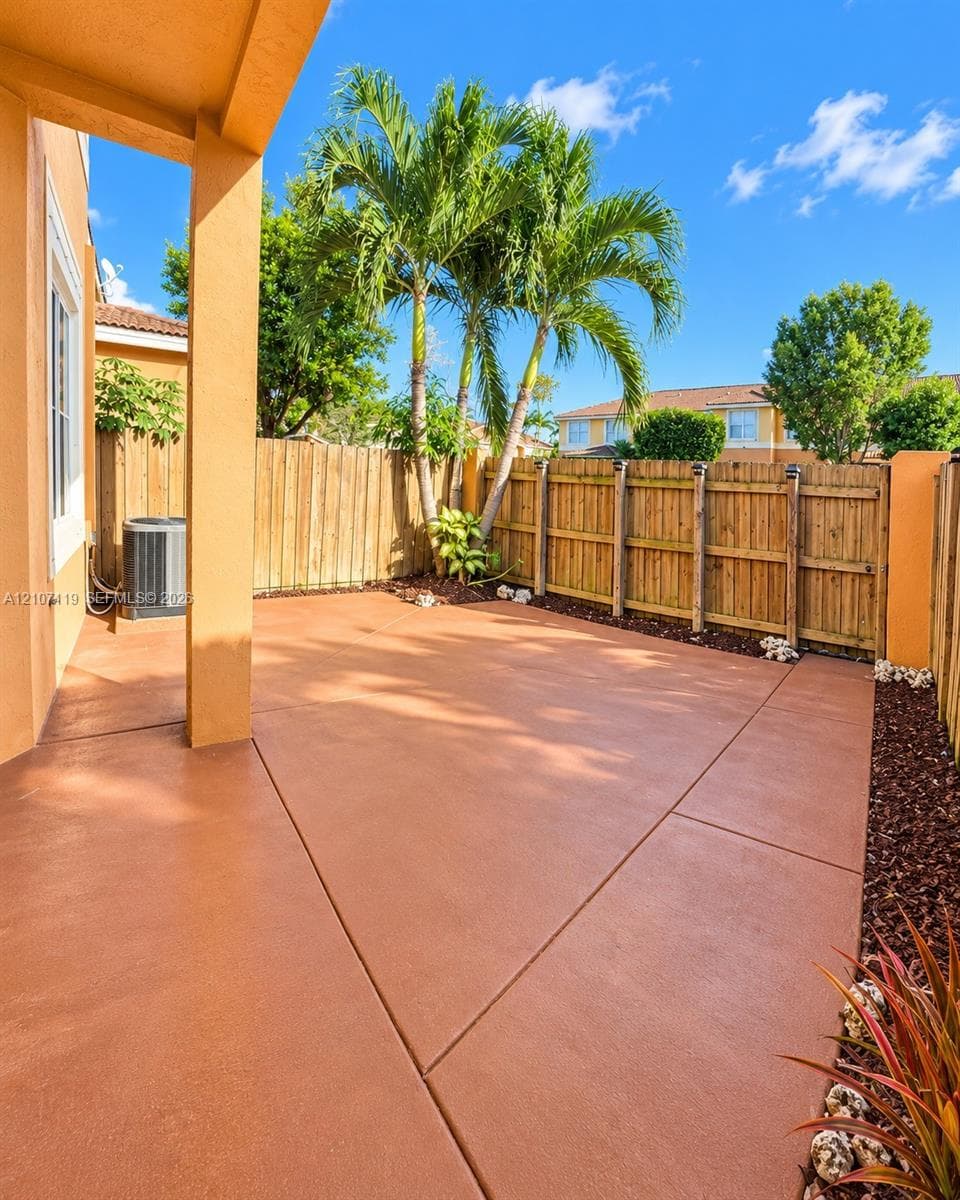 Covered patio featuring a scored concrete floor, wood-plank fencing, and palm trees