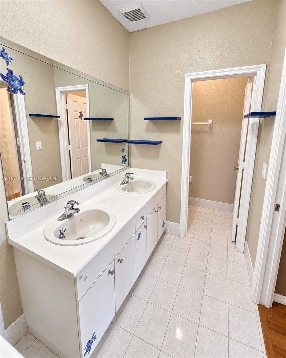 Dual-sink vanity featuring a solid surface countertop, inset basins, chrome-finish faucets, and large wall-mounted mirror