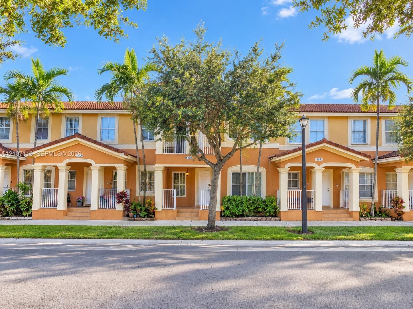 Mediterranean-style townhome exterior featuring a red tile roof, arched entryway columns, second-story balconies, and private covered porch entries