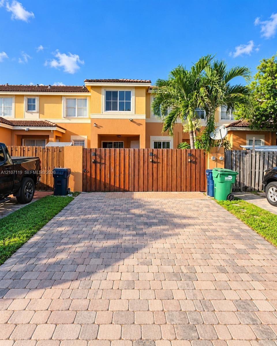 Two-story exterior with stucco finish, paver driveway, and wood-slat privacy fencing