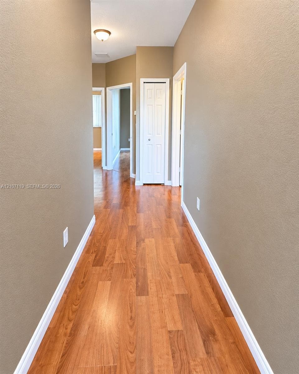 Hallway featuring wood-finish flooring, neutral wall paint, and white bi-fold closet doors
