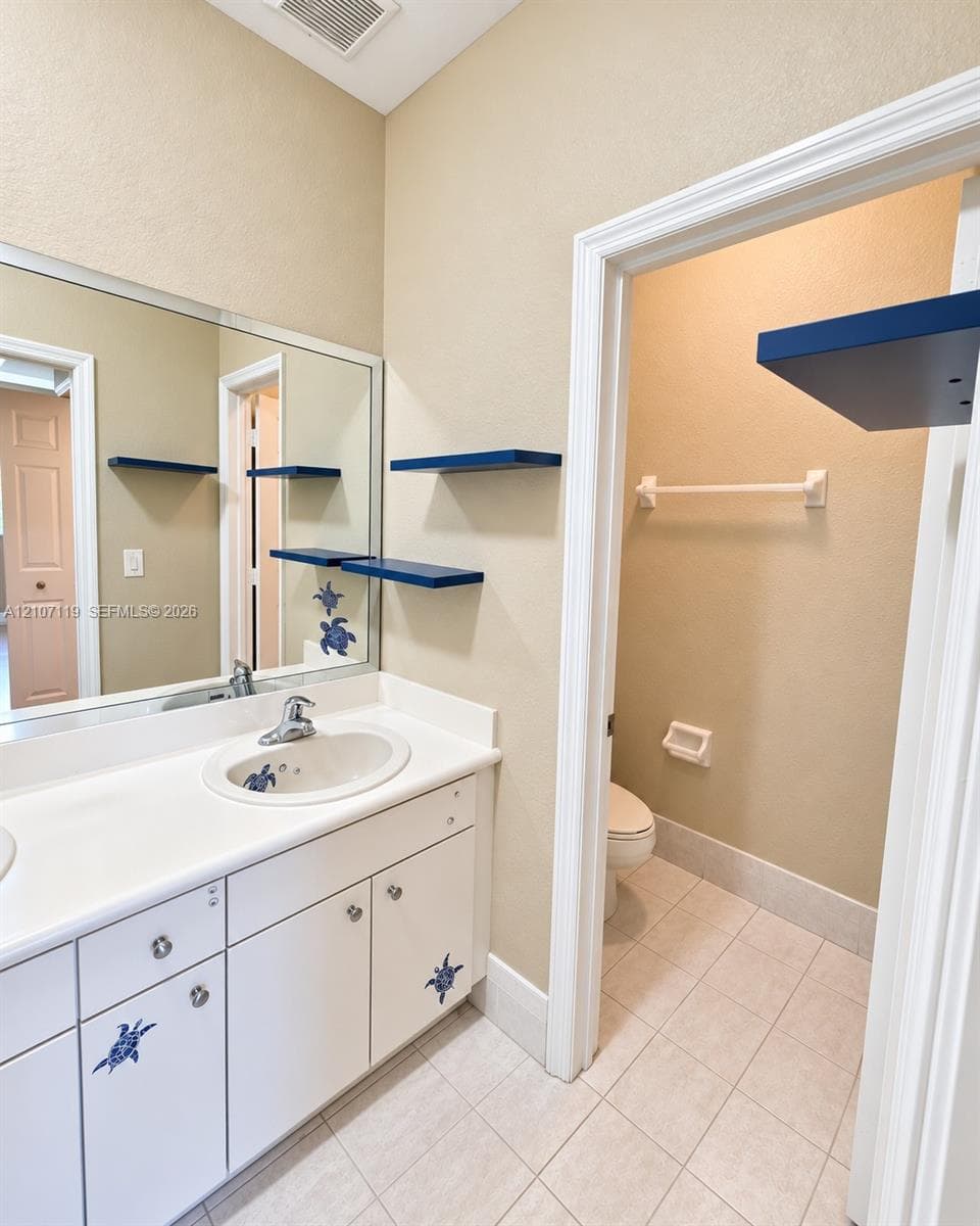White vanity with integrated basin, solid-surface countertop, full-width mirror, and ceramic tile flooring