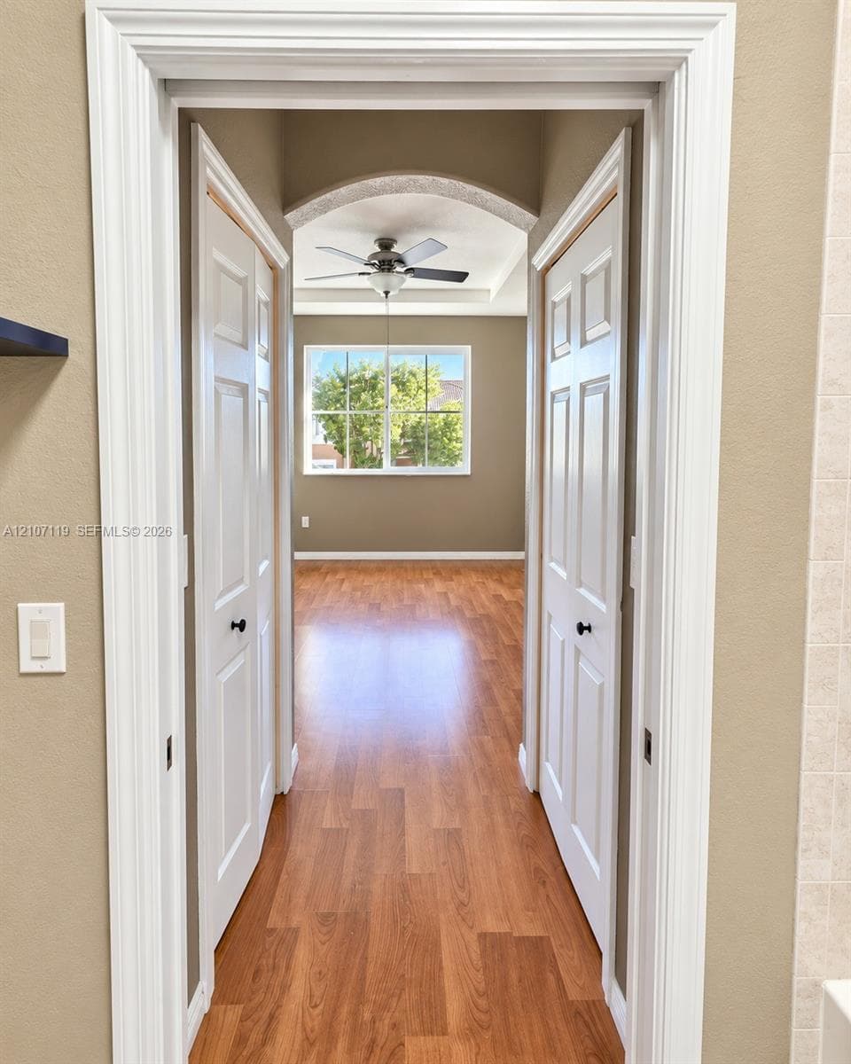 Arched doorway with white casing, wood-finish flooring, two six-panel swing doors, and a ceiling fan with integrated lighting