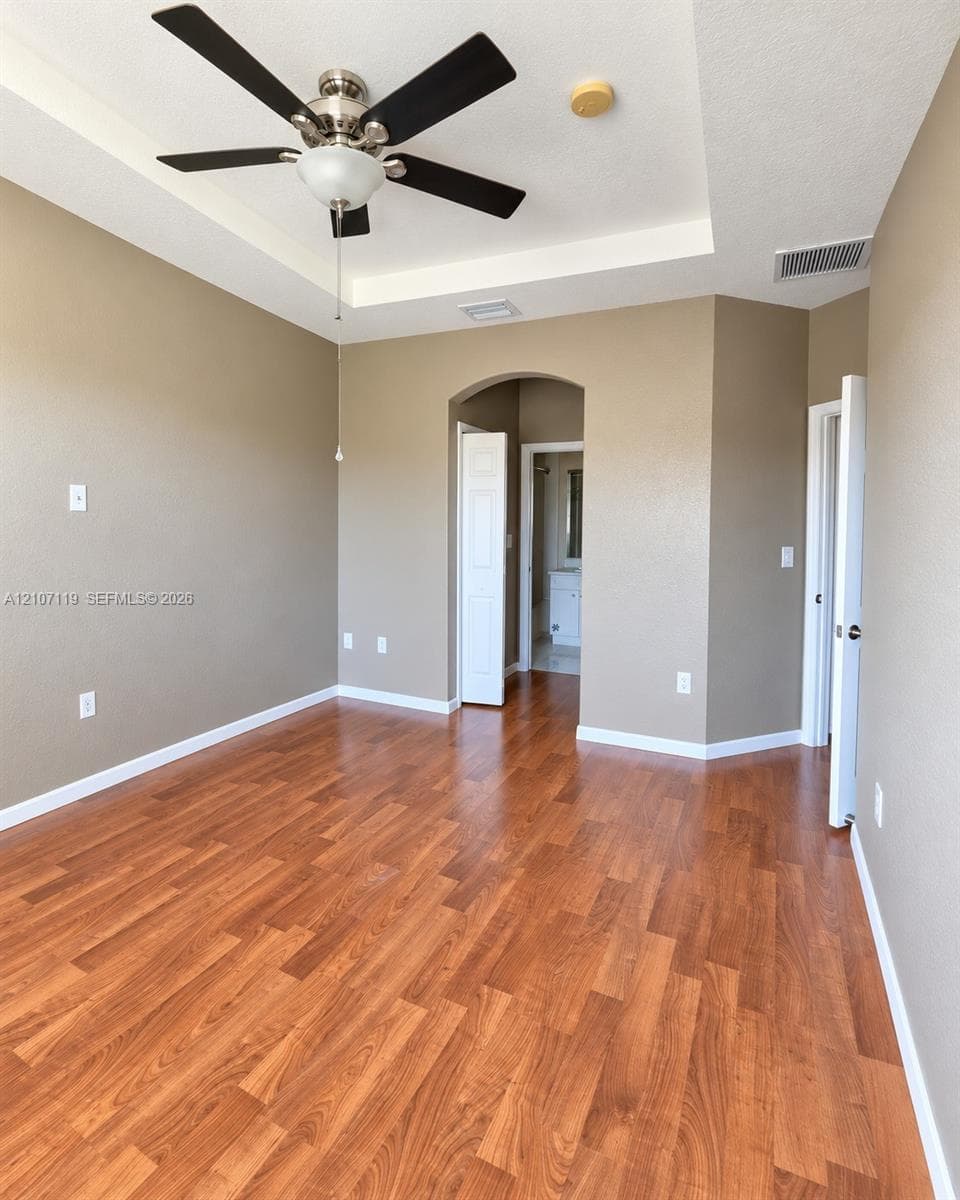 Tray ceiling, multi-blade ceiling fan with integrated lighting, and wood-finish flooring