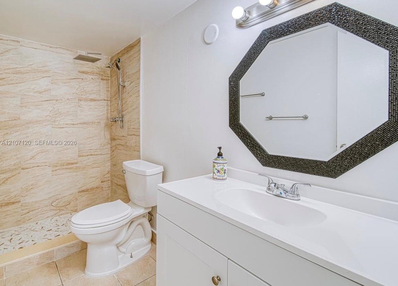 Bathroom featuring a vanity with a white countertop and oval under-mount sink, tiled shower enclosure with a rain-style showerhead, and an octagonal wall-mounted mirror