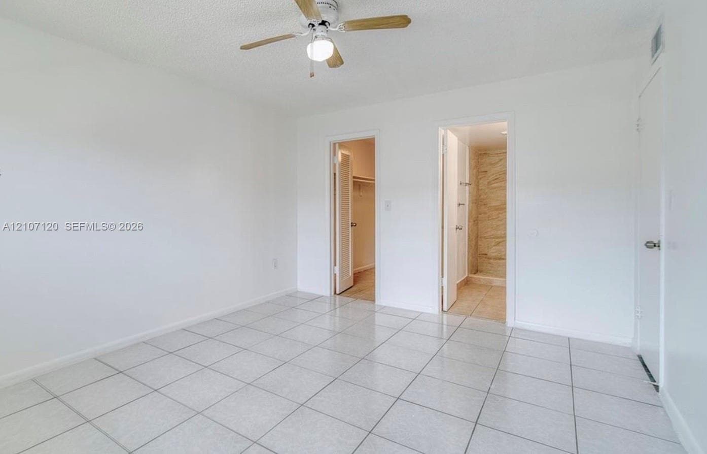 Neutral ceramic tile flooring, ceiling fan with integrated light, walk-in closet, and tile-lined shower stall