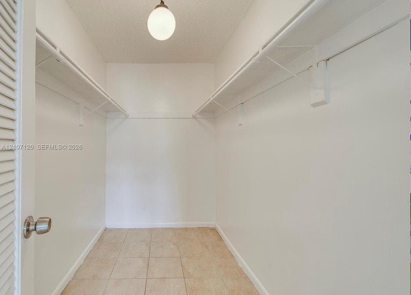 Storage space featuring white walls, tiled flooring, dual-level wire shelving, and a globe-style overhead light fixture