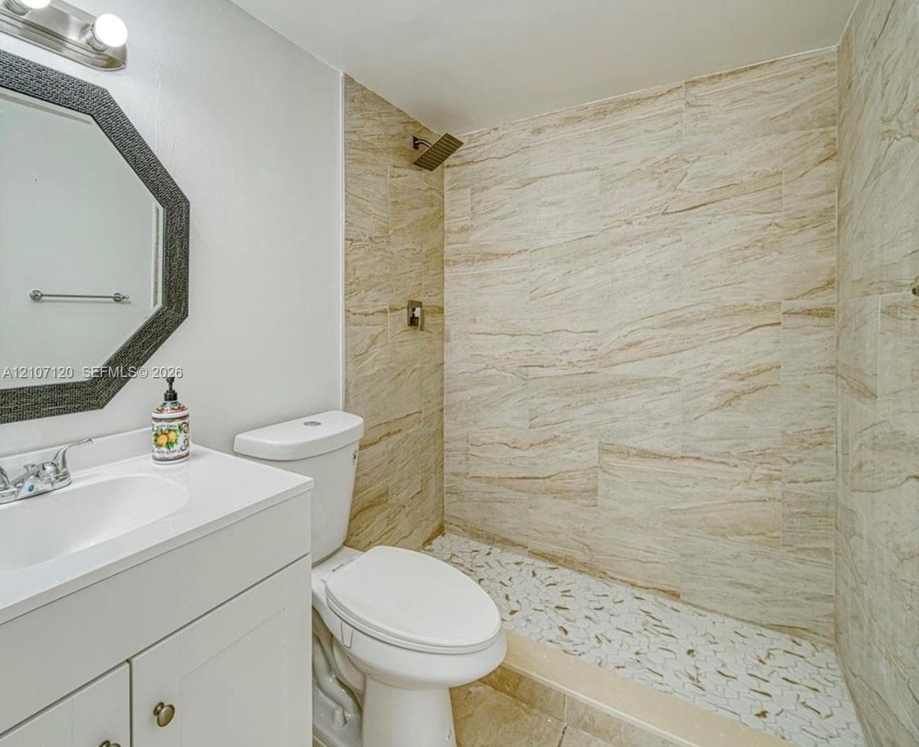 Bathroom featuring a vanity with an integrated sink, octagonal wall-mounted mirror, walk-in shower with stone-tile surround, and mosaic-tile shower floor