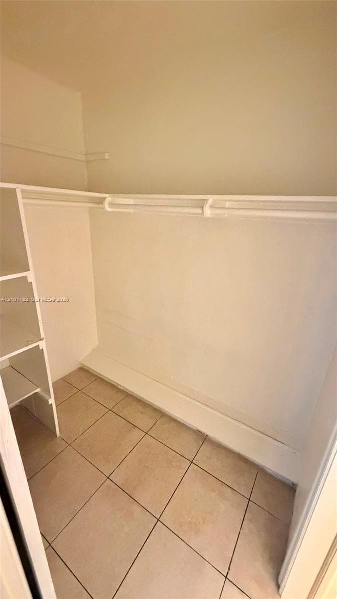Reach-in closet featuring white built-in shelving, an integrated hanging rod, a floor-level storage shelf, and tile flooring