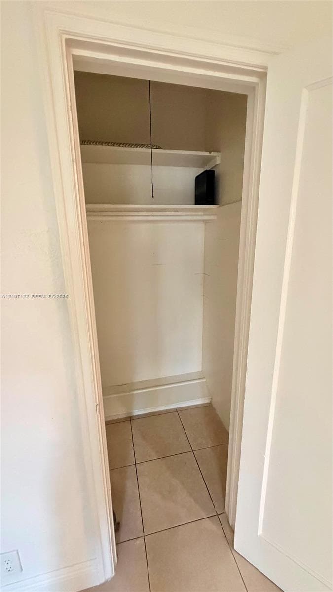 Storage closet featuring tile flooring, a built-in overhead shelf, and a hanging rod