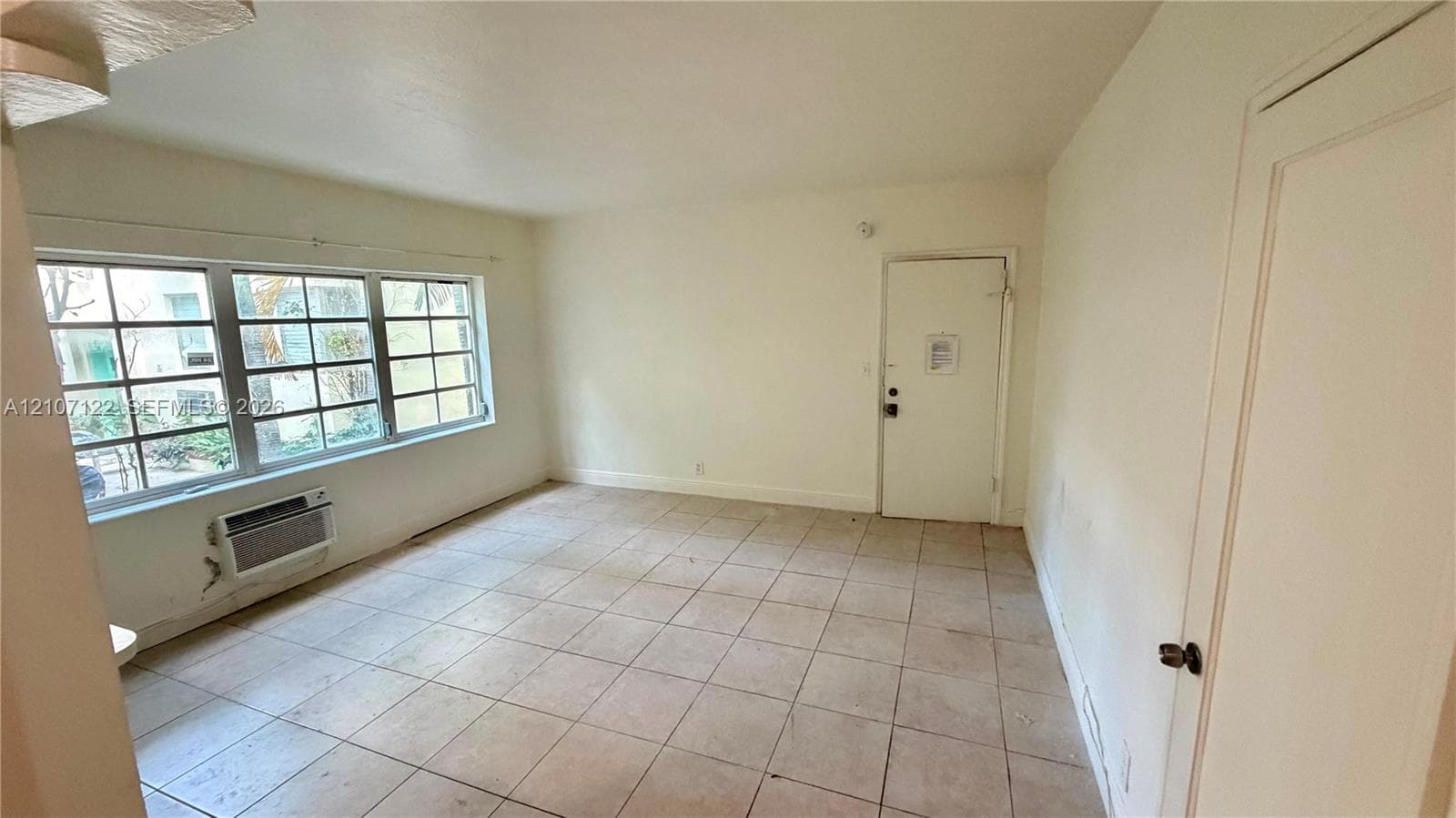 Interior room featuring large multi-pane windows, neutral tile flooring, and a wall-mounted climate control unit
