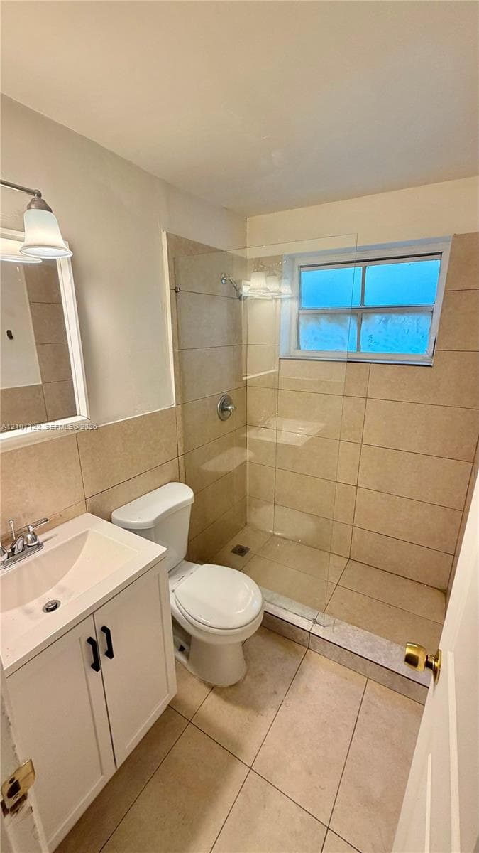 Bathroom featuring a walk-in shower with a glass panel, large-format wall and floor tile, vanity with a white cabinet, and a wall-mounted light fixture
