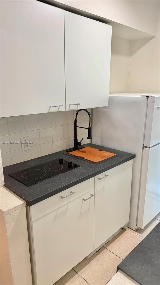 Kitchenette featuring white cabinetry, dark stone-finish countertops, a two-burner electric cooktop, and a matte black gooseneck faucet with tiled backsplash