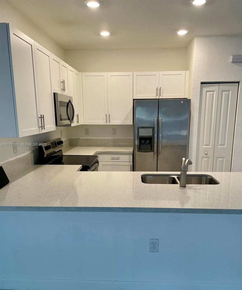 Kitchen featuring white shaker-style cabinetry, solid-surface countertops, recessed lighting, stainless steel appliances, and a dual-basin undermount sink
