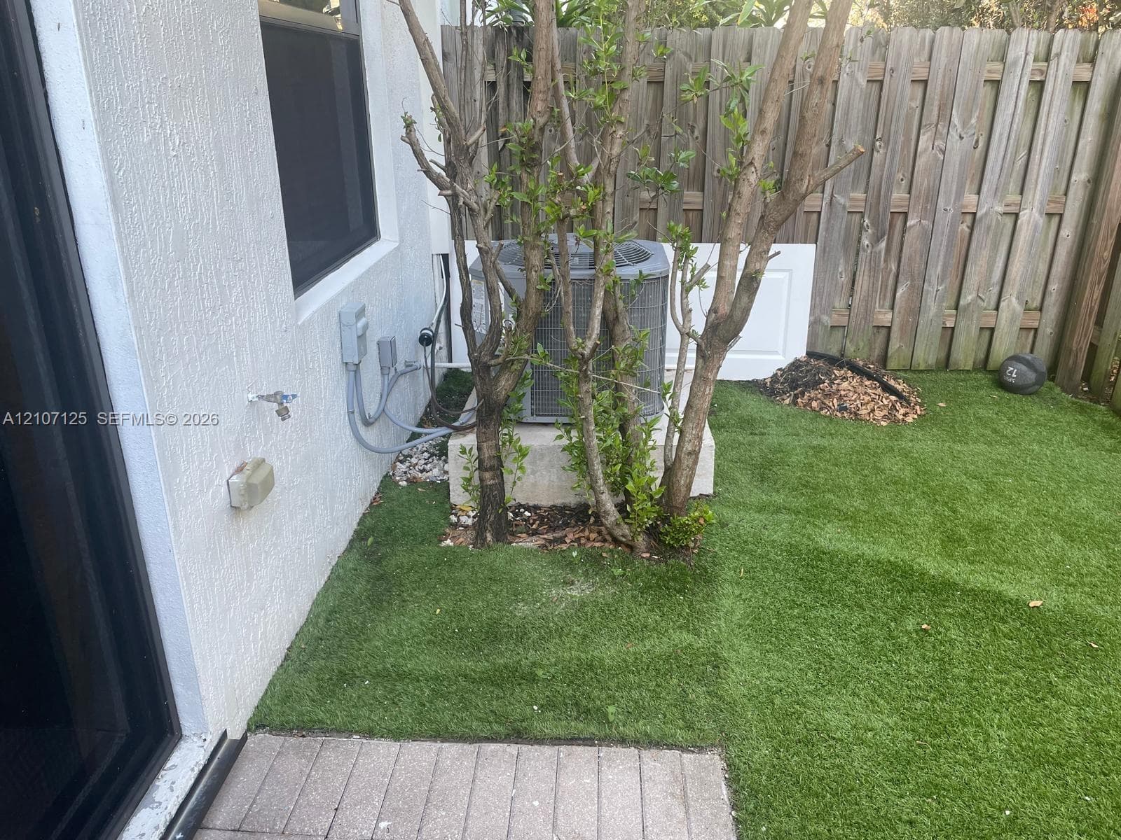 Exterior area featuring synthetic grass, wood-plank privacy fencing, and concrete paver patio surface