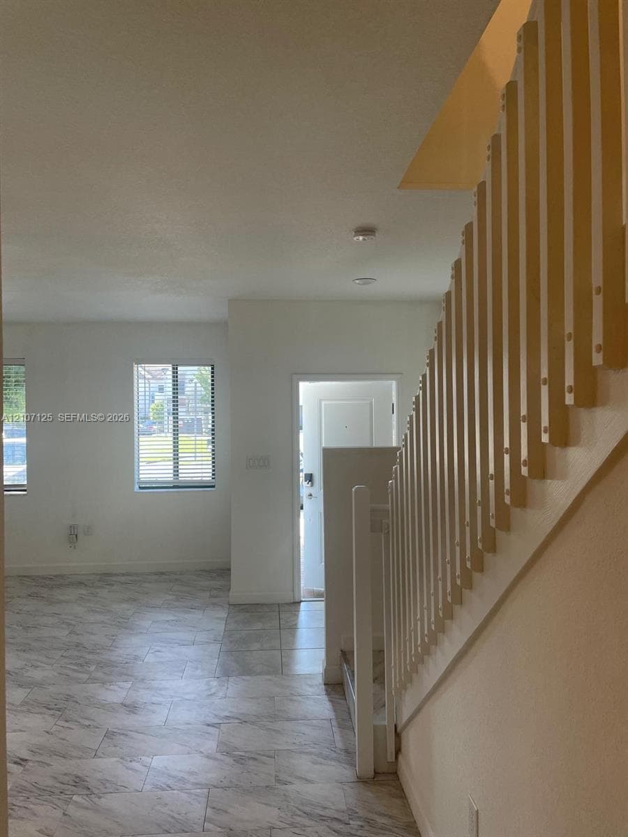 Staircase featuring vertical wood slat railings, stone-finish tile flooring, and windows with integrated blinds