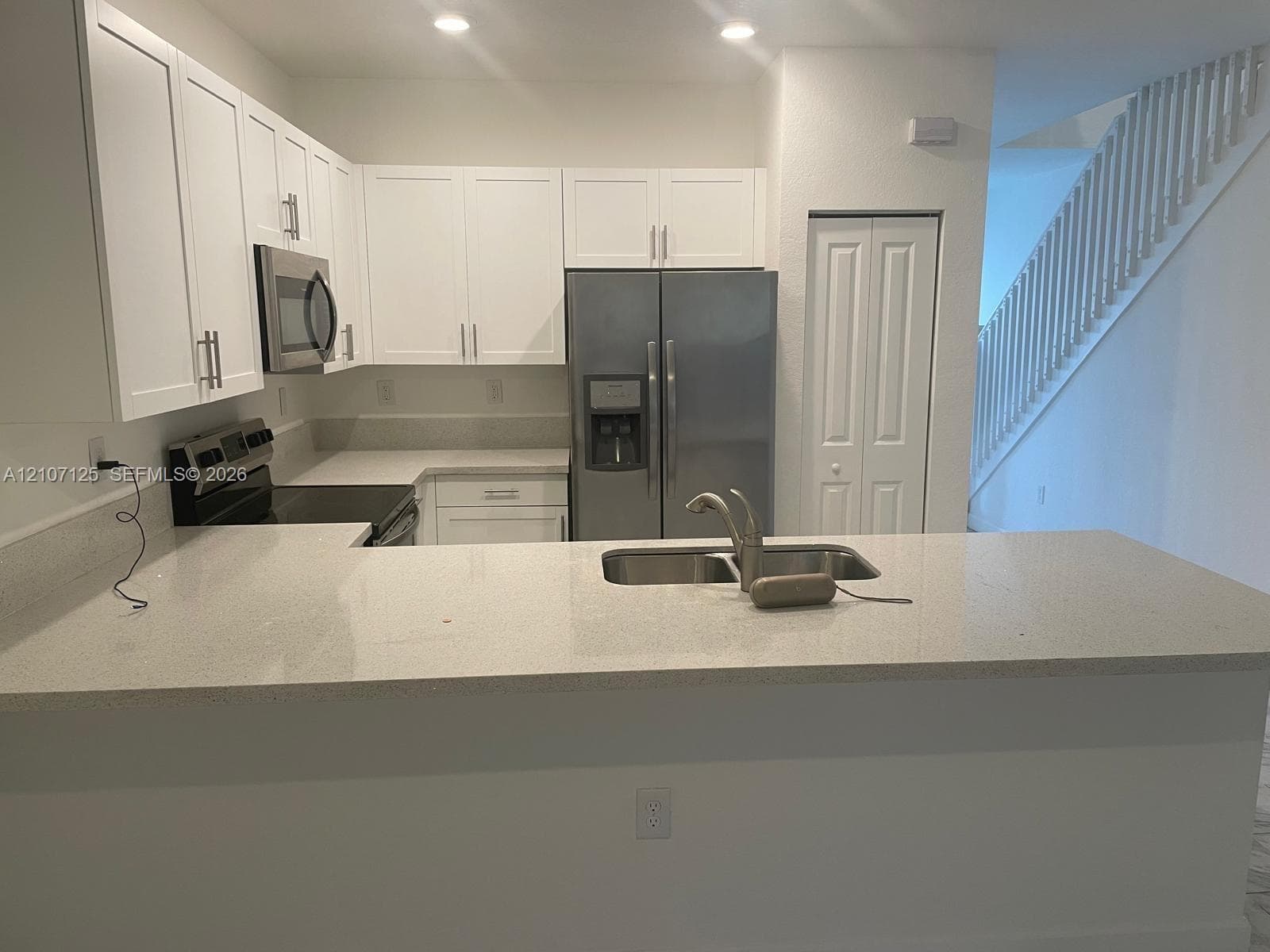 Kitchen featuring white cabinetry, solid-surface countertops, stainless steel appliances, and a double-basin undermount sink