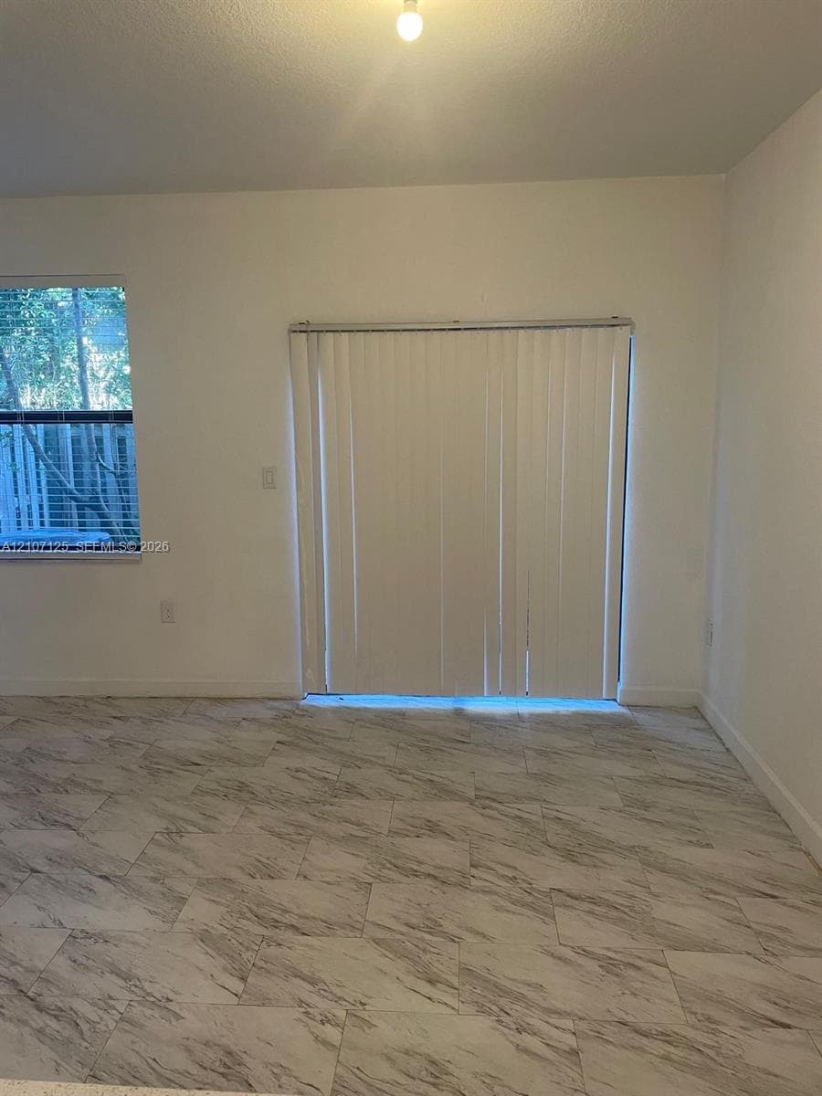 Neutral interior featuring large-format stone-patterned tile flooring, vertical window blinds, and natural light exposure