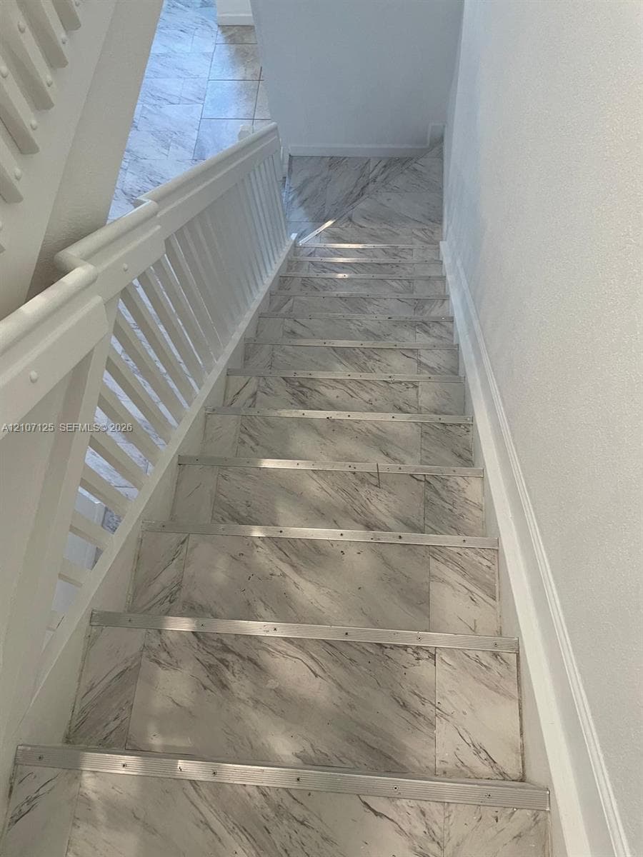 Staircase featuring stone-finish treads, metallic edge nosing, and white wooden balusters