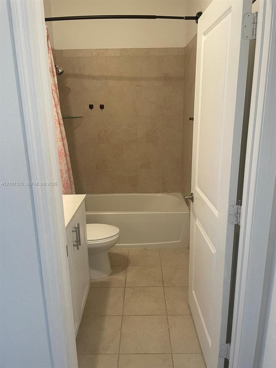 Bathroom featuring a tub-shower combination with tile surround, white vanity cabinet, tiled flooring, and a two-panel interior door