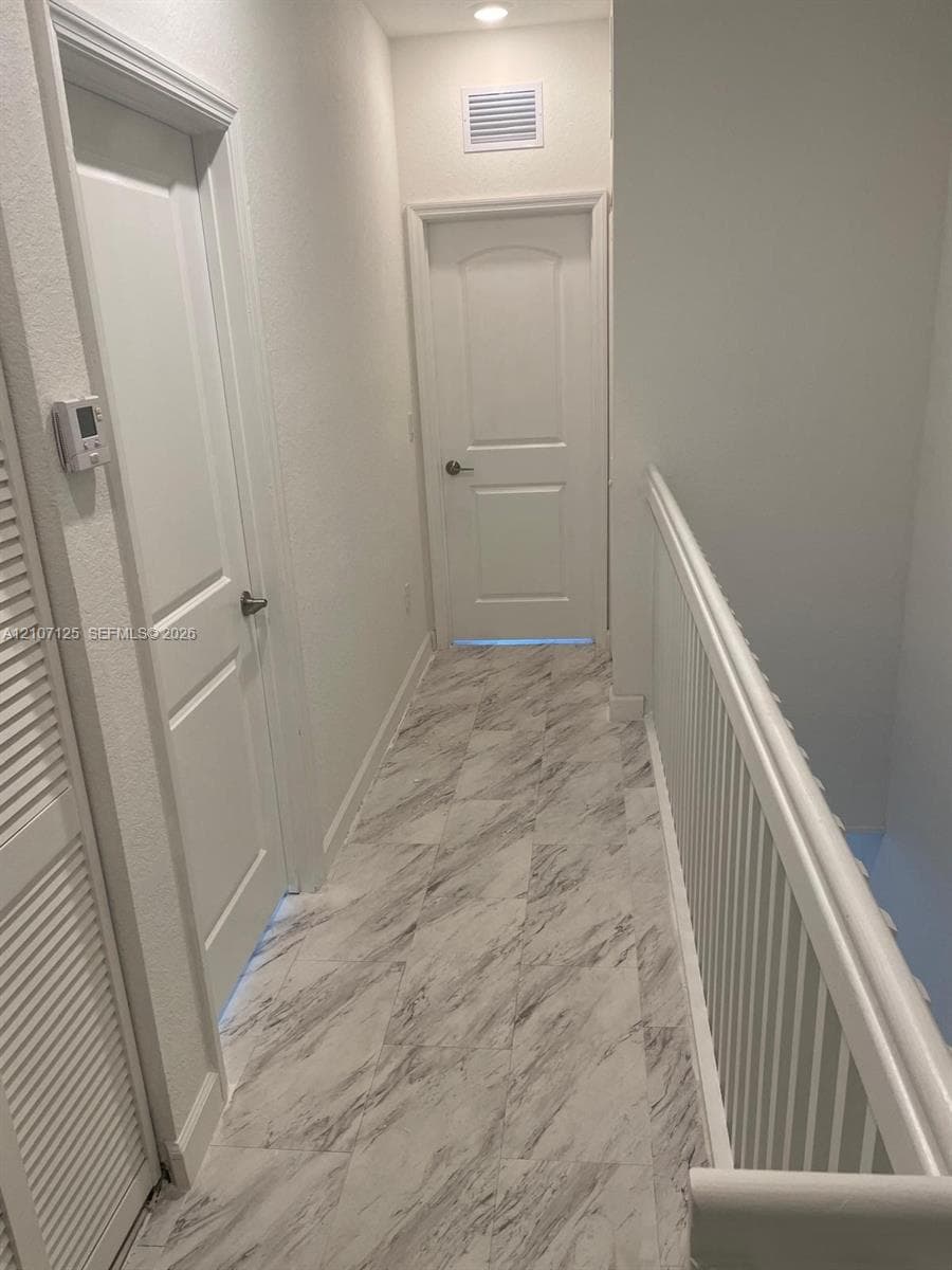 Hallway featuring stone-patterned tile flooring, white two-panel doors with metallic hardware, and a white baluster railing