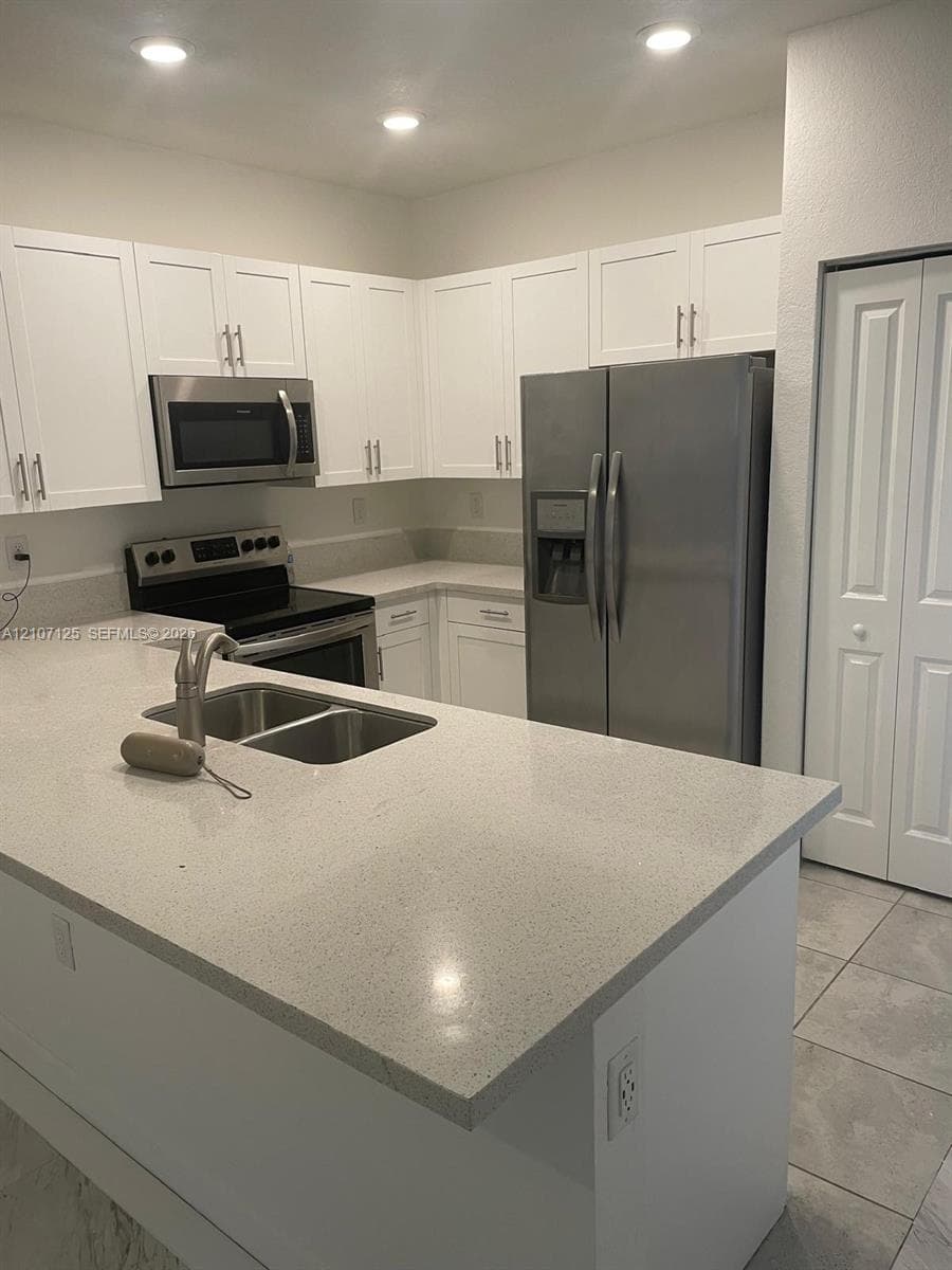 Kitchen featuring white shaker-style cabinetry, solid-surface countertops, a stainless steel dual-basin undermount sink with a high-arch pull-down faucet, and a suite of stainless steel appliances