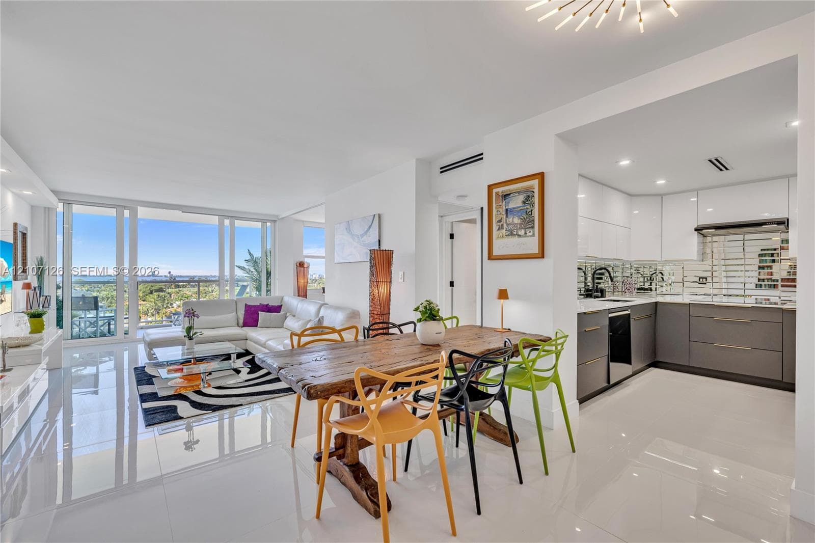 Open-concept living space featuring high-gloss tile flooring, floor-to-ceiling glass panel windows, recessed lighting, and a modern kitchen with dual-tone cabinetry and metallic backsplash