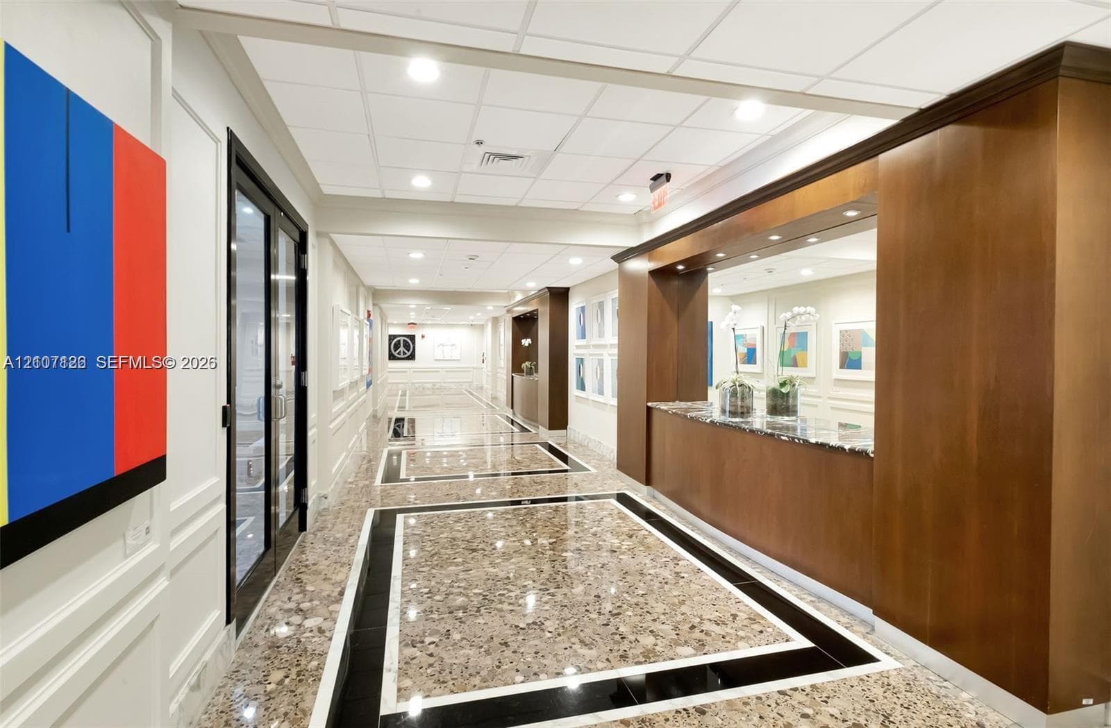 Lobby featuring polished stone flooring with geometric inlays, custom wood-paneled reception desk with stone countertop, recessed lighting, and wall molding
