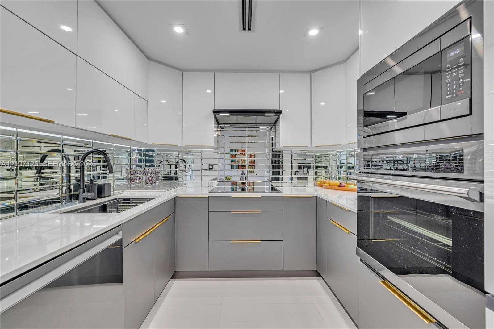 Kitchen featuring high-gloss cabinetry, stone-surface countertops, mirrored tile backsplash, integrated stainless steel appliances, and gold-finish hardware