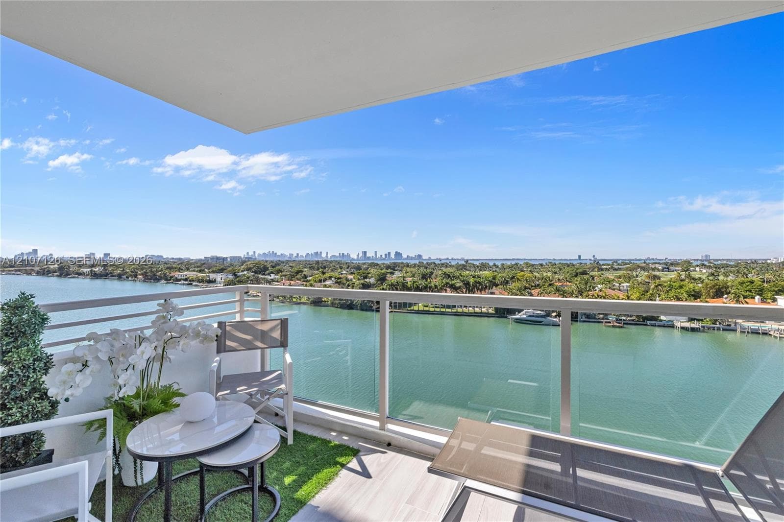 Private balcony featuring glass-panel railings and tile flooring overlooking the waterway and city skyline