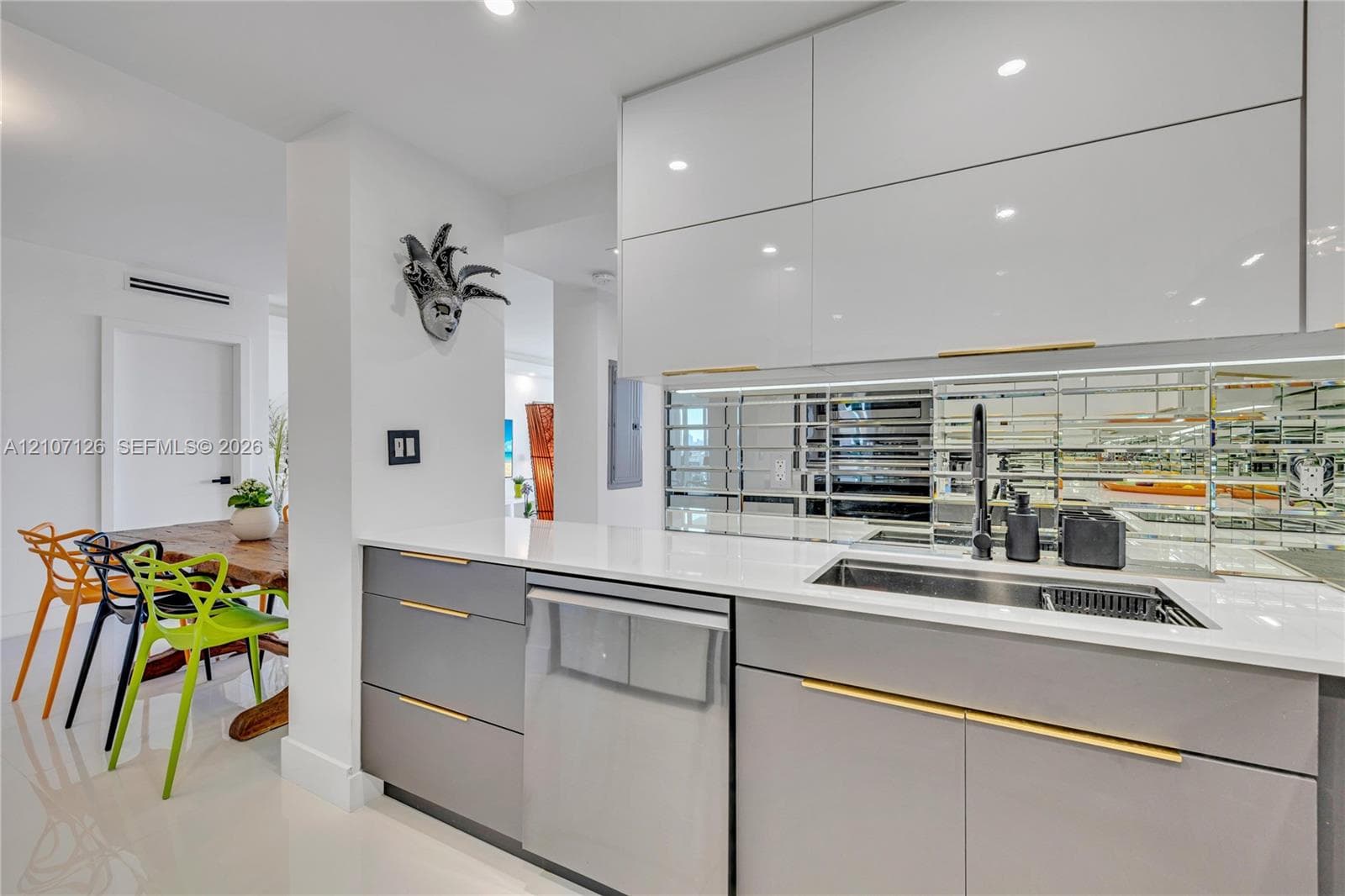 Kitchen featuring high-gloss cabinetry, stone countertops, mirrored tile backsplash, undermount sink with a matte black faucet, and brass-tone hardware