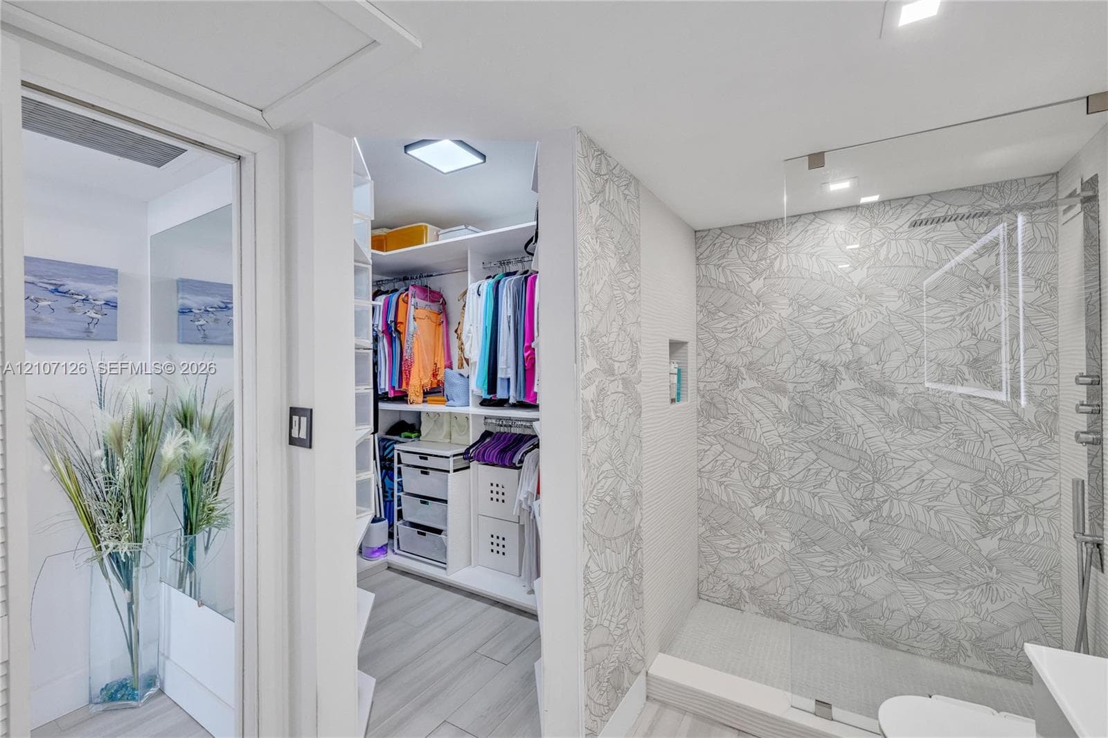 Walk-in closet featuring built-in shelving and drawer units, accompanied by a tiled shower with patterned wall detailing, a recessed shower niche, a frameless glass enclosure, and recessed lighting