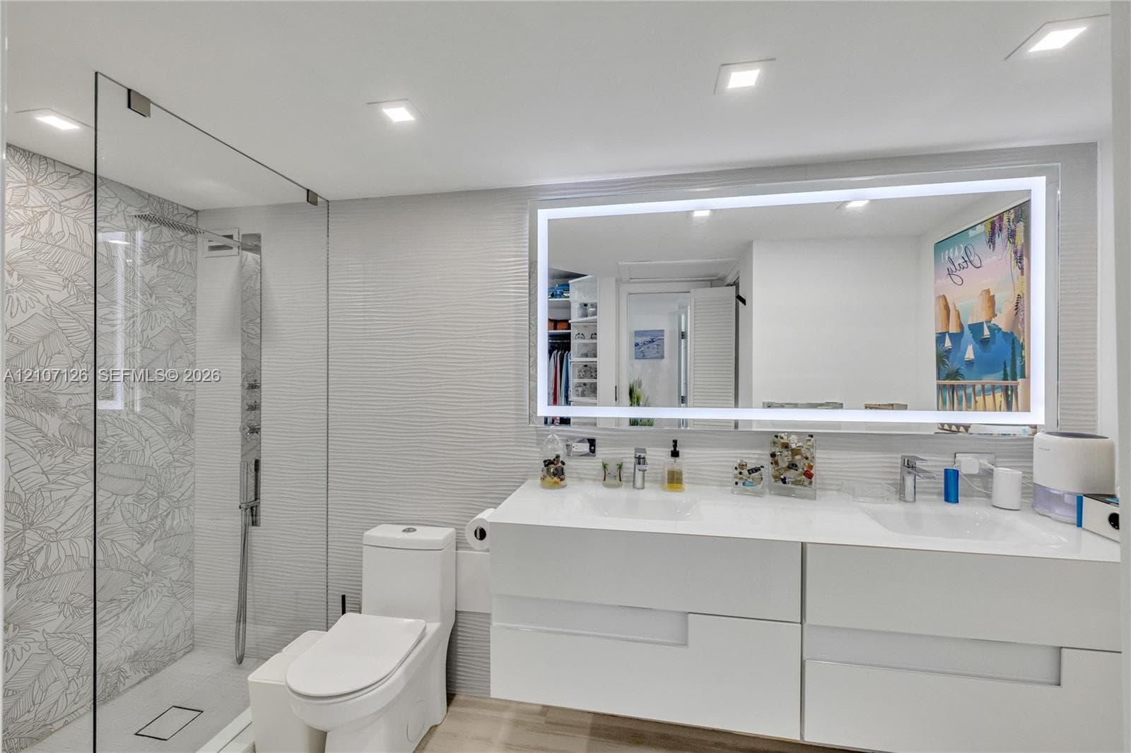 Floating dual-sink vanity with a solid-surface countertop, glass-enclosed walk-in shower with decorative tile detailing, large LED-backlit mirror, and recessed ceiling lighting