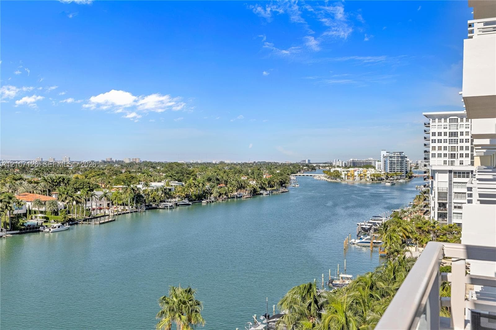 Elevated balcony featuring a glass and metal railing overlooking a wide waterway, coastal residential landscape, and horizon