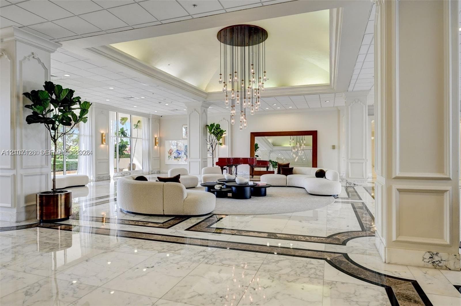 Grand lobby featuring tray ceilings, multi-tiered pendant lighting, decorative columns with millwork, and polished stone flooring with intricate geometric inlays